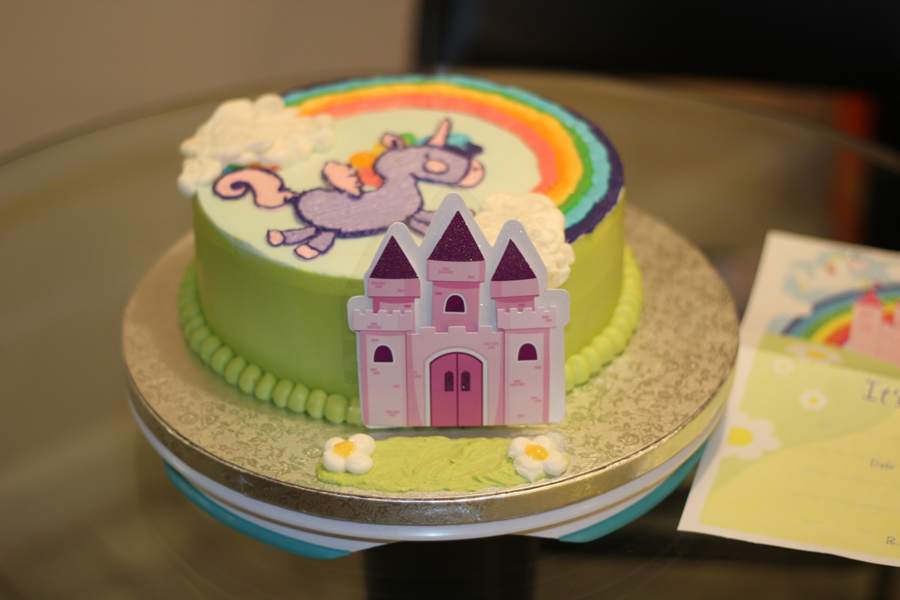 The finished unicorn cake on a gold board, rainbow arcing over the top and a castle set into the side